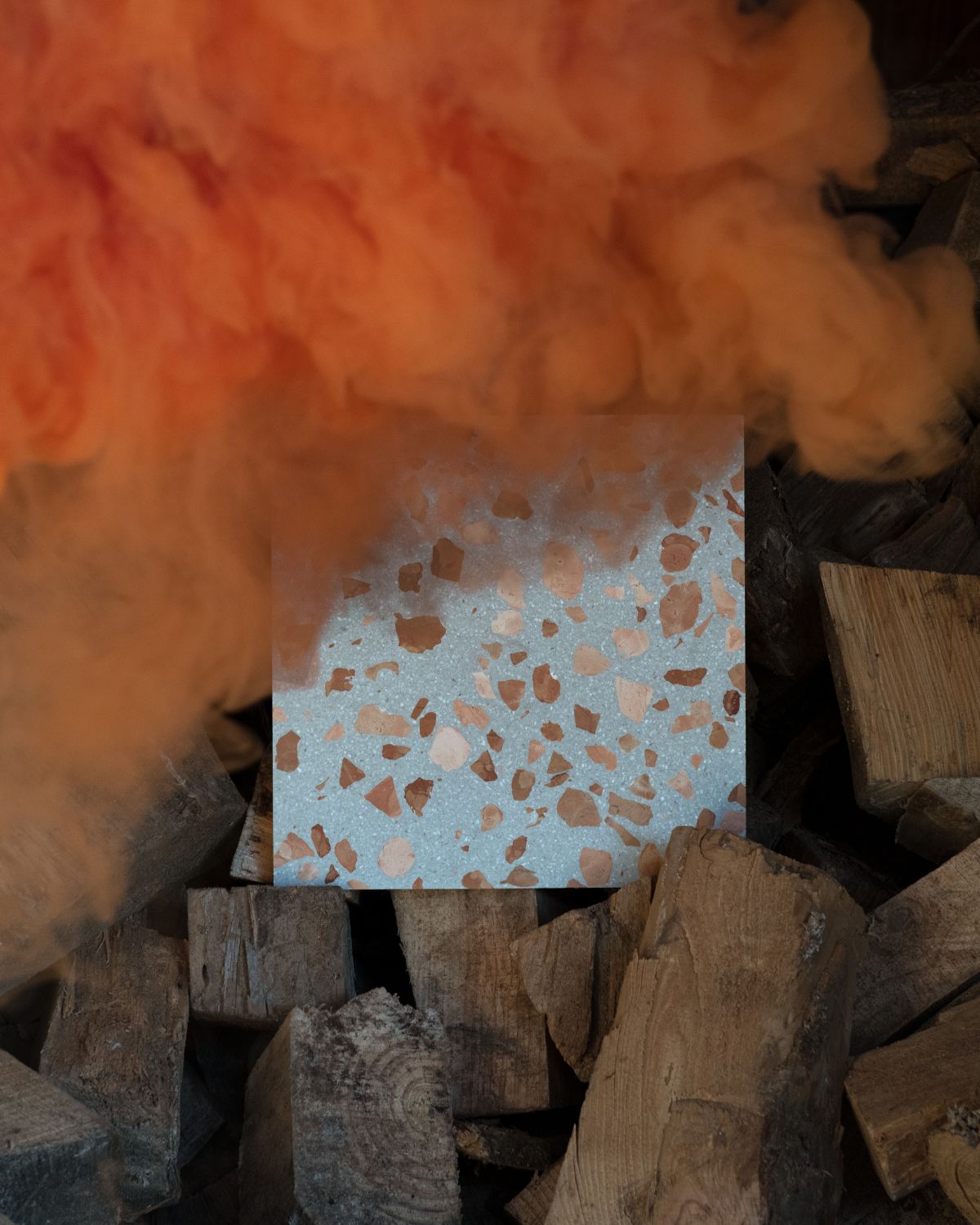 Terrazzo tile with a gold leaf pattern surrounded by wooden blocks and orange smoke.